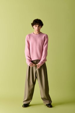 Yakışıklı adam kendine güvenerek parlak bir odada duruyor, şık pembe bir kazak ve rahat bir pantolon giyiyor..