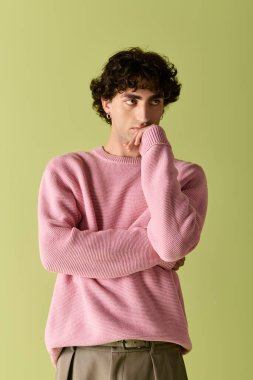 Kıvırcık saçlı yakışıklı adam zarif pembe bir kazak içinde özgüven saçıyor..