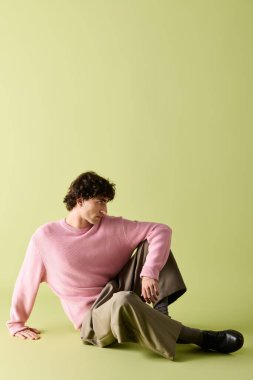 Yakışıklı adam açık pembe bir süveter ve şık bir pantolon giyiyor, düşünceli bir şekilde oturuyor..