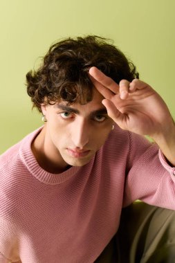 Pembe süveter giyen genç adam yerde otururken neşeli bir jest yapıyor..