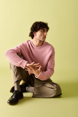 Cesur genç bir adam zarif bir şekilde yeşil bir zemine yaslanmış, moda anlayışını sergiliyor..