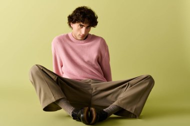 Yakışıklı adam modaya uygun giyiniyor, yumuşak yeşil arka planda güvenle oturuyor..