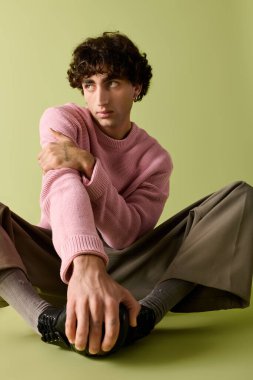 Modern kıyafetlerle, yumuşak yeşil bir arka planda, şık bir birey poz verir..