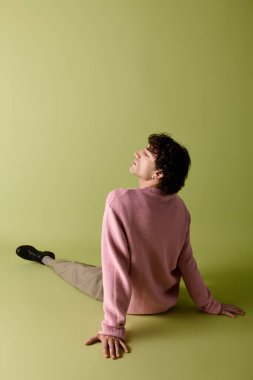 Pembe kazaklı şık bir adam zarif bir şekilde yeşil bir zemine karşı poz verir..