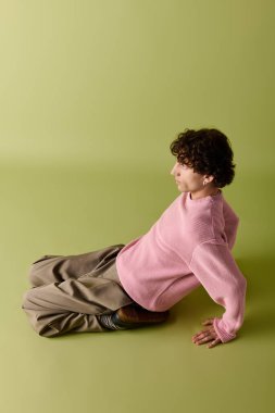 Pembe kazaklı ve bej pantolonlu yakışıklı adam yeşil arka planda tarzını sergiliyor..