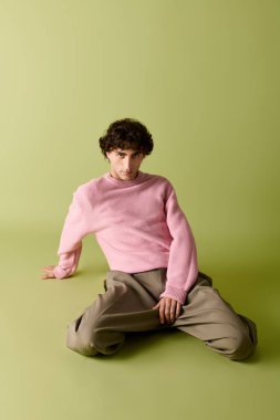 Yakışıklı bir adam, yumuşak yeşil bir arka fona karşı pastel pembe bir kazakla güvenle poz verir..