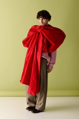 Yakışıklı bir adam kendine güvenerek stüdyoda duruyor, çarpıcı kırmızı bir fiyonk ve eşsiz bir kıyafet giyiyor..