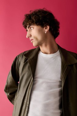 Şık giyinmiş yakışıklı bir adam, tarzını sergileyen kalın pembe bir duvara karşı duruyor..