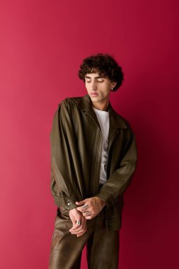 Şık bir adam kendine güvenerek ayakta duruyor, çarpıcı kırmızı bir arka plana karşı şık bir kıyafet giyiyor..