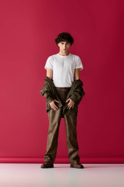 Yakışıklı bir adam gururla beyaz gömlekli ve kahverengi pantolonlu tarzını gösterir..