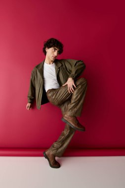 Moda kıyafetleri içinde yakışıklı bir adam kırmızı bir arka plana karşı duruyor, şık bir poz veriyor..