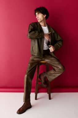 Yakışıklı adam, ahşap bir taburede şık kıyafetler sergiliyor. Karizma ve yetenek saçıyor..