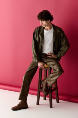 Şık bir kıyafet giymiş yakışıklı bir adam bir taburede oturup moda anlayışını ön plana çıkarıyor..