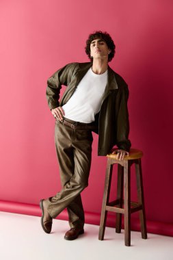 Yakışıklı bir şahıs, şık bir kıyafet ve çarpıcı bir duruş sergileyen bir tabureyle zarif bir poz verir..