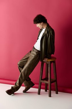 Şık bir adam bir tabureye yaslanır, parlak bir arka plana karşı elbisesini gösterir..