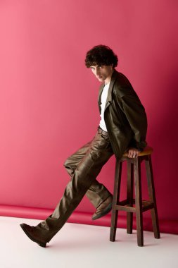 Şık bir beyefendi, modaya uygun giyinmiş, kendine güvenen bir şekilde bir taburede poz verir..