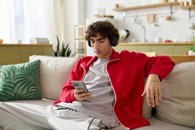 Kıvırcık saçlı yakışıklı adam şık bir kanepede rahatlar ve telefonundan müzik dinler..