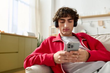 Moda giyinmiş yakışıklı bir adam koltukta otururken telefonuyla müzik dinliyor..