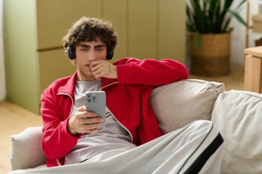 Moda kıyafetli genç adam akıllı telefonuyla modern, davetkar bir mekanda takılıyor..