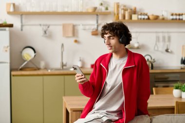 Moda kıyafetleri içinde yakışıklı bir adam telefonuyla müzik dinliyor. Etrafı şık bir mutfakla çevrili..