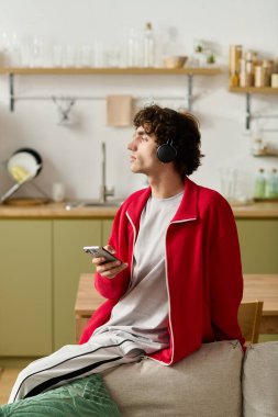 Moda kıyafetli yakışıklı adam rahat bir mutfakta telefonundan müzik dinliyor..