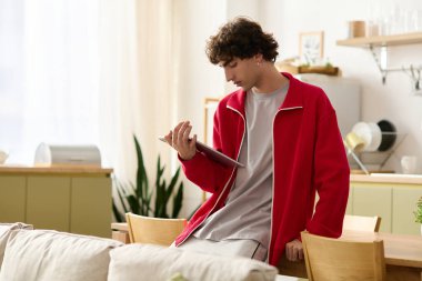 Kırmızı ceketli yakışıklı bir adam, evinde rahat bir dekorla çevrili bir tablet okurken rahatlıyor..