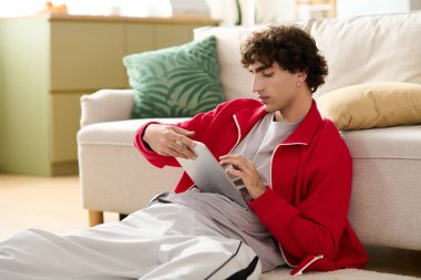 Şık bir genç adam yerde dinleniyor, rahat bir oturma odasında tabletine odaklanıyor..