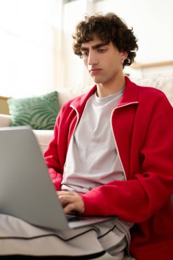 İyi giyimli bir adam evde rahat otururken dizüstü bilgisayarına odaklanmış..