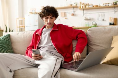 Moda kıyafetleri içinde yakışıklı bir adam, akıllı telefonuyla rahat bir şekilde koltukta oturur..