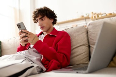 Moda kıyafetli yakışıklı bir adam evde rahat bir öğleden sonra bir koltukta oturup telefonunu kullanıyor..