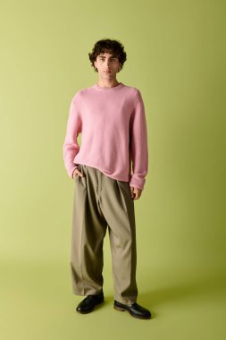 Yakışıklı bir adam yeşil bir zemine karşı yumuşak pastel renklerle modaya uygun kıyafetler sergiliyor.