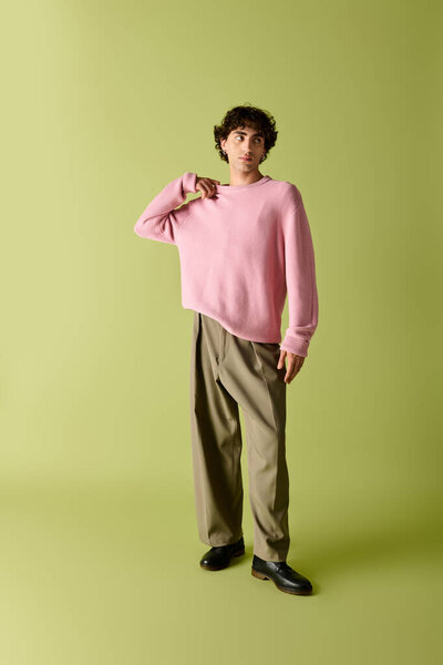 Красивый мужчина в розовом свитере и без штанов уверенно стоит с игривым взглядом.