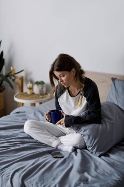 Genç bir kadın, sıcak mekanında dinlenirken mavi bardaktan yudumlayarak gününün tadını çıkarır..