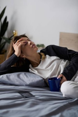 Kadın yatağında uzanıyor, elinde bir fincanla dinleniyor, evinde sakin bir günü kucaklıyor..