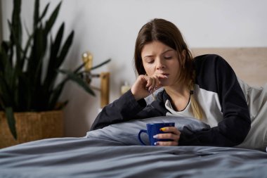 Genç bir kadın, modern bir dairede sıcak bir bardak tutarken, düşünceler içinde kendini kaybediyor..