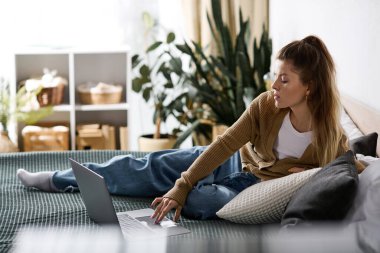 Genç bir kadın gününü yatağında rahat bir şekilde laptopunu karıştırarak geçirir..