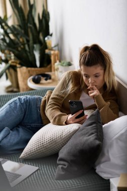 Gününü yatakta geçiren genç bir kadın modern bir mekanda telefonunu yansıtıp kaydırıyor..