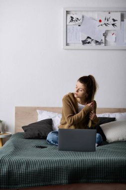 Bir kadın rahat bir ortamda yatağında oturur, tek başına dinlenirken görevlerini yapar..