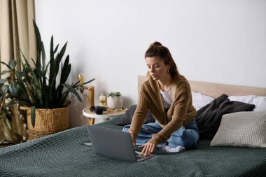 Genç bir kadın yatakta dinleniyor, şık bir dairede dizüstü bilgisayarını kullanıyor, tembel bir günü kucaklıyor..