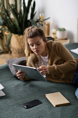 Genç bir kadın, şık bir yatak odasında kitap okuyup su içmekten zevk alır..