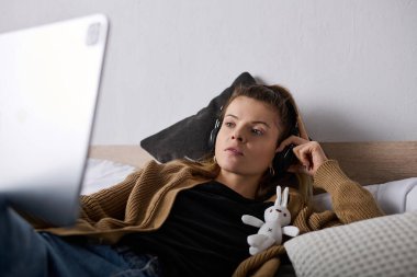 Genç bir kadın zamanını yatakta müzik dinleyerek ve evinde dinlenerek geçirir..