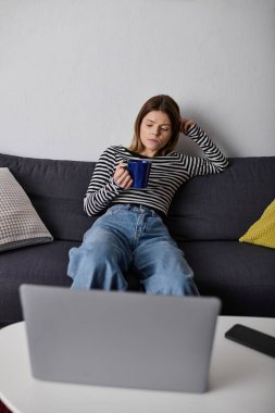 Genç bir kadın bir içkiyle kanepede dinleniyor, evde huzurlu bir günün tadını çıkarıyor..