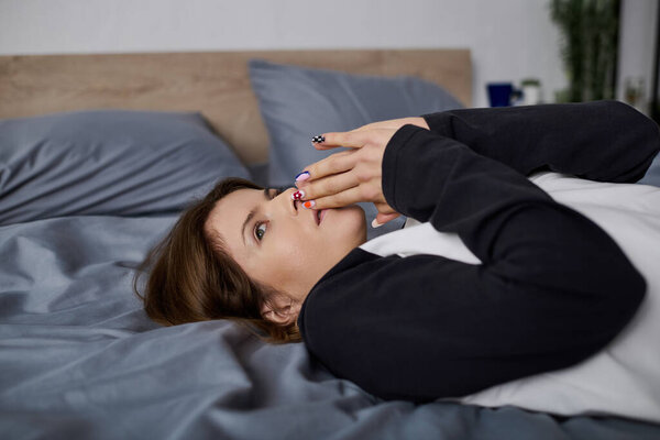 A young woman relaxes alone in bed, finding comfort during a burnout phase in her modern apartment.
