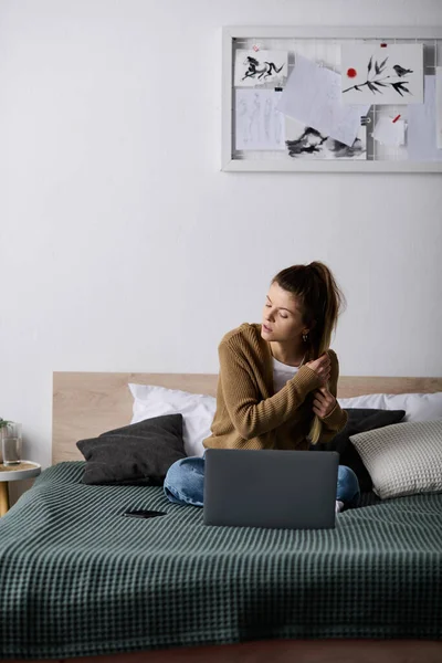 Bir kadın rahat bir ortamda yatağında oturur, tek başına dinlenirken görevlerini yapar..