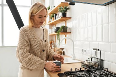 Rahat kıyafetler giymiş bir kadın modern mutfağında rahat bir içecek hazırlar..