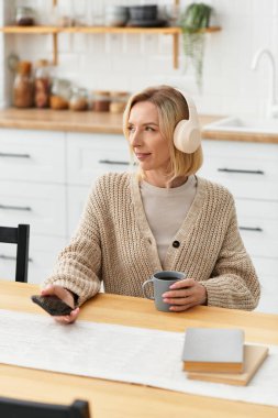 Sarışın kadın rahat dairesinde dinleniyor, müzik dinlerken sıcak bir içkinin tadını çıkarıyor..