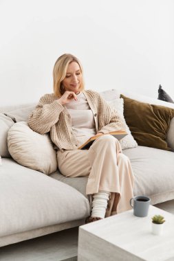 Sarışın kadın modern bir dairede rahat rahat rahat kitap okuyor..