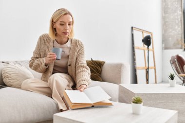 Sarışın kadın evinde dinleniyor, çay içiyor ve kışın rahat bir şekilde kitap okuyor..