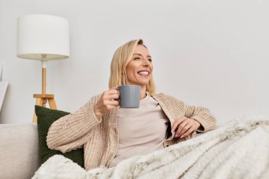 Bir kadın rahat hırkasıyla rahatlar, sıcak bir içecek yudumlar, kapalı alanda mutlu anları kucaklar..