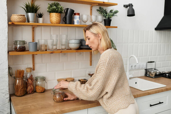 A woman in comfortable clothing prepares a snack in her stylish kitchen, embracing a laid-back mood.